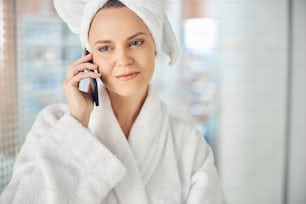 Close up portrait of a serious female with a bath towel on her head calling on her smartphone