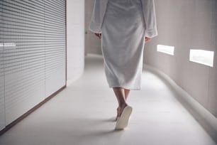 Foto ritagliata di una signora in pantofole che cammina lungo il corridoio in un salone termale