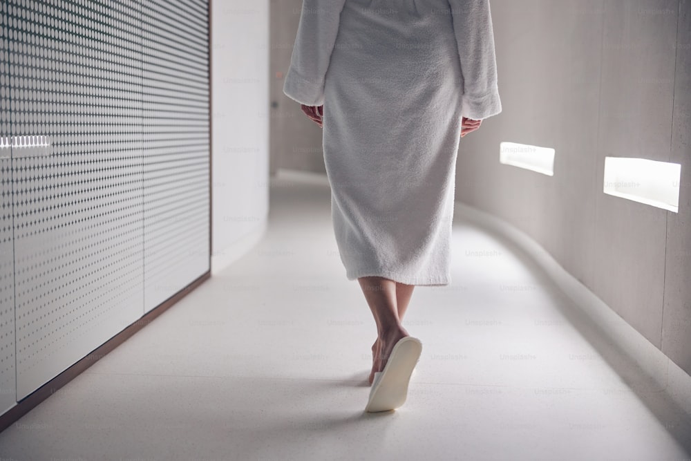 Foto recortada de una señora en pantuflas caminando por el pasillo en un salón de spa