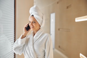 Waist-up portrait of a female with her hair wrapped in a towel talking on the smartphone