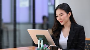 Donna d'affari asiatica che legge le notizie sulla tavoletta digitale mentre è seduta in un ufficio moderno.