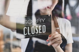 Woman coffee shop owner turning closed sign board on glass door.