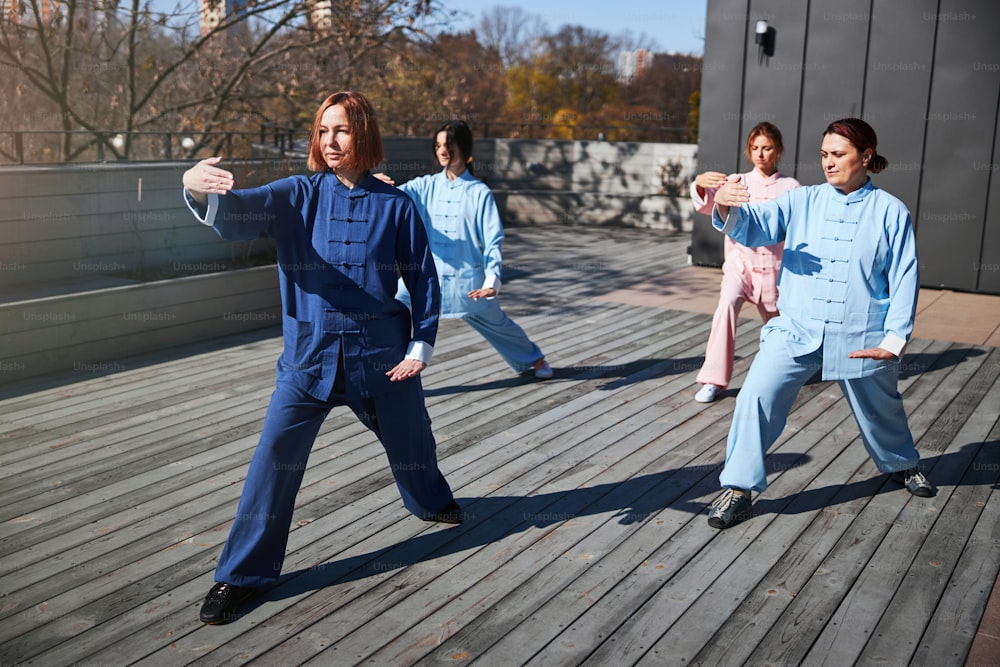 Three women working with their master and practicing qigong outdoors on a sunny day