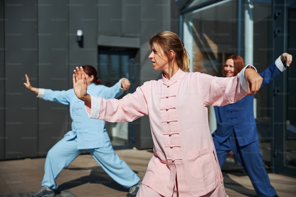 Three women standing in specific postures on a sunny terrace while working out with qigong