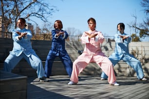 Cuatro mujeres jóvenes concentradas de pie en posturas específicas con los pies abiertos mientras se ejercitan para las artes marciales chinas