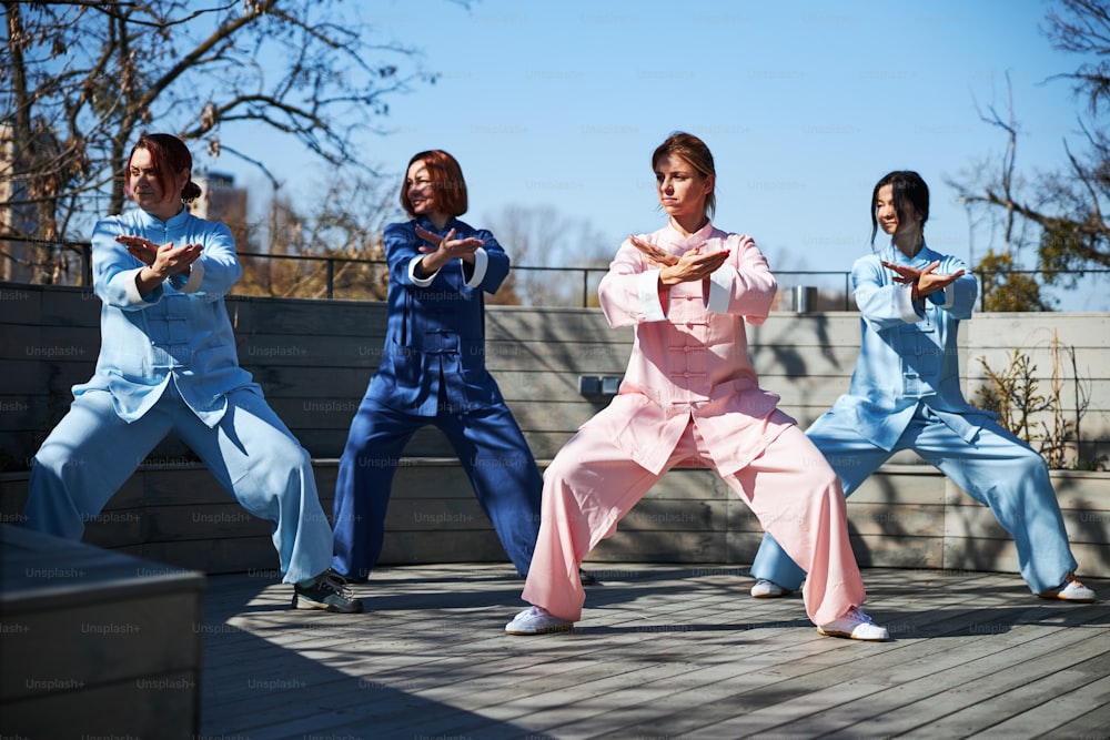 Quattro giovani donne concentrate in piedi in posture specifiche con i piedi larghi mentre si allenano per le arti marziali cinesi
