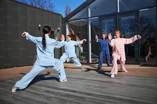 Group of people in Chinese suits training martial arts outdoors on a terrace. Qigong or tai chi concept