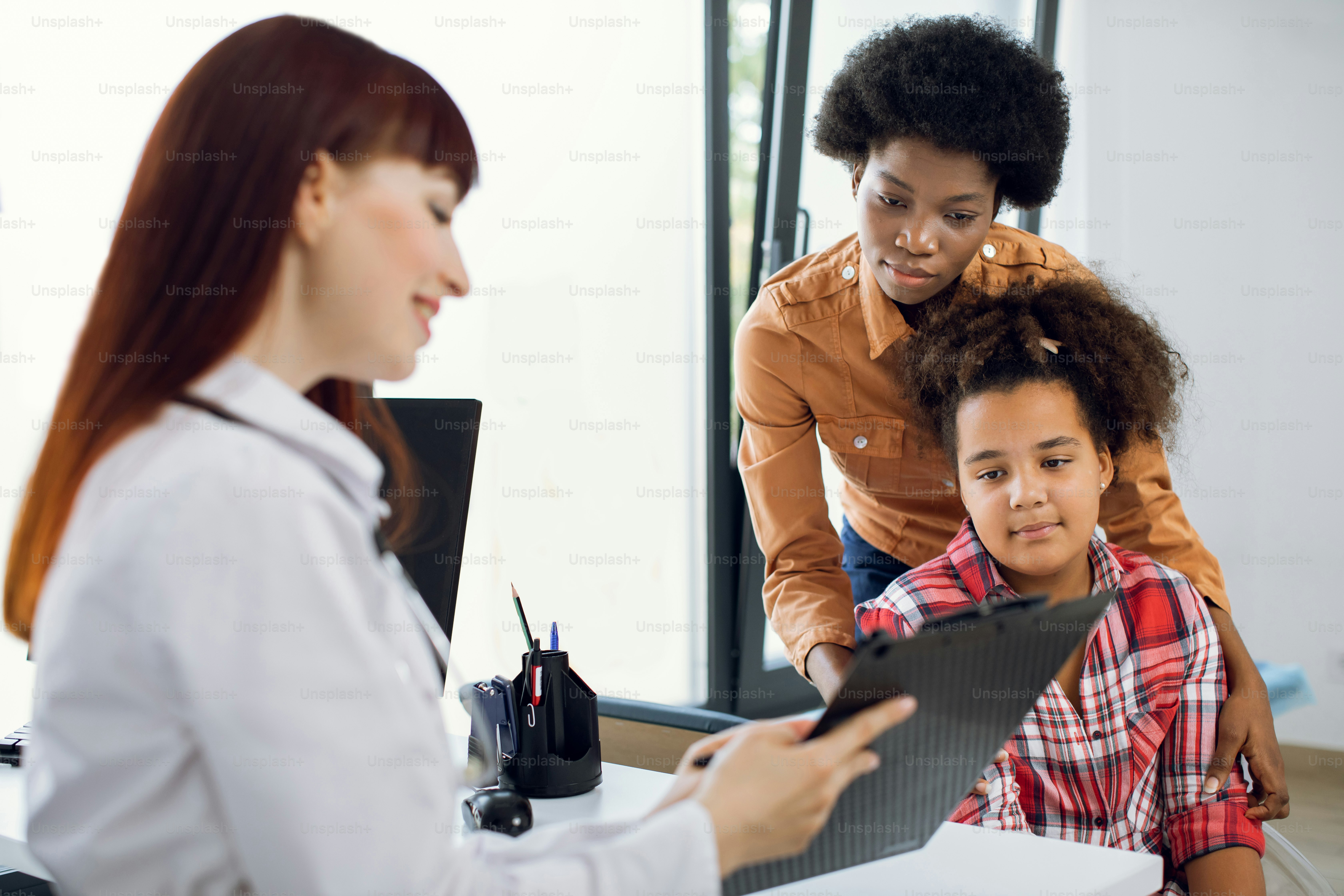 Pediatra medico donna che mostra il referto medico o i risultati dei test  medici alla giovane madre africana e alla sua figlia di dieci anni su un  blocco per appunti in una, image size:3000x2000