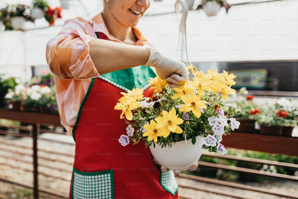 Mulher adulta jovem feliz e positiva que trabalha na estufa e desfruta de belas flores.