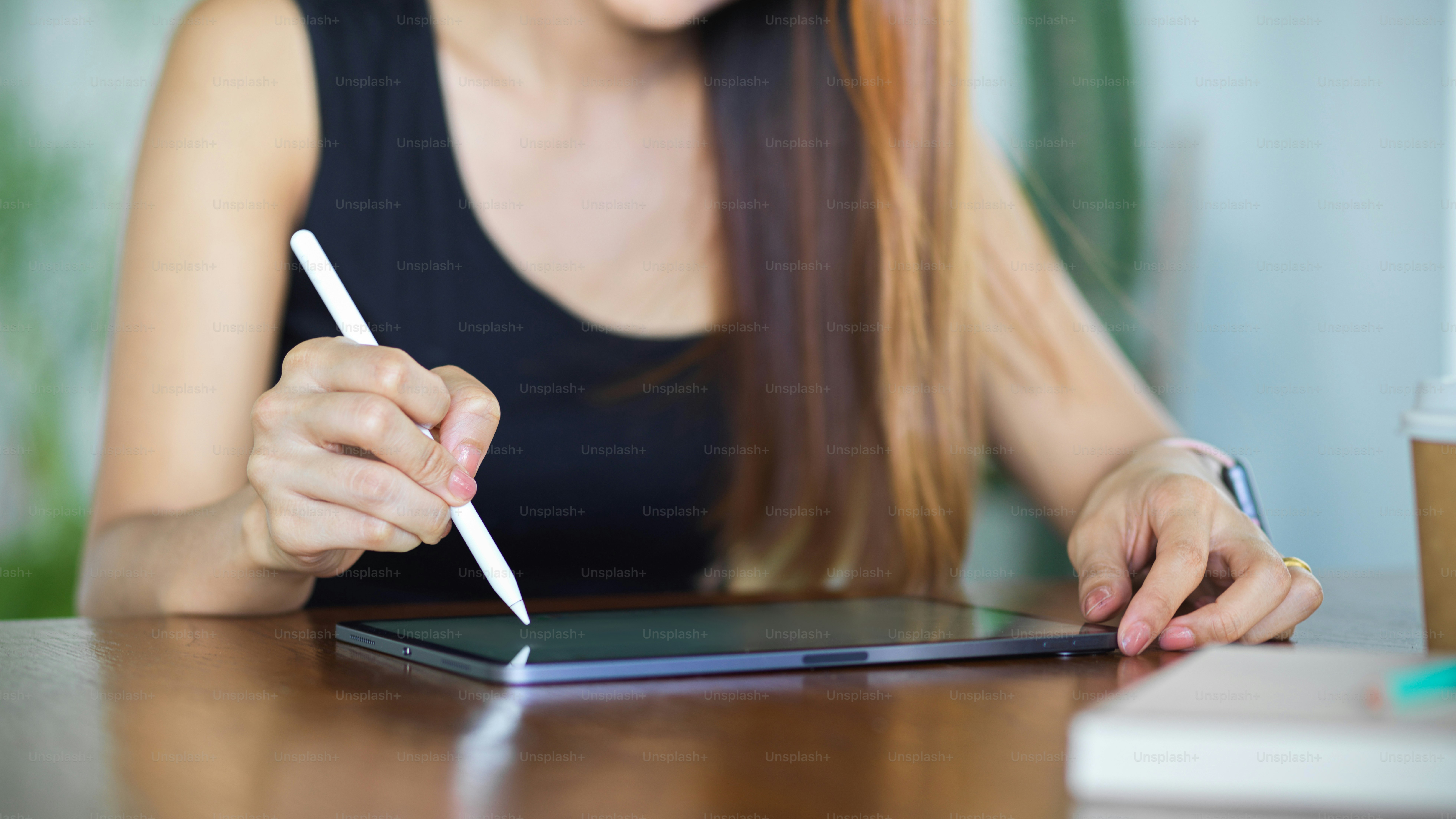 Cropped shot of young female hand with stylus pen touching on digital tablet screen on wooden table