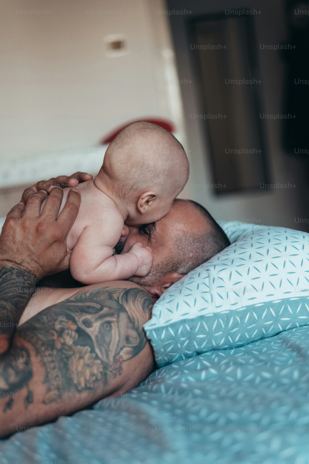 Tattooed bearded father playing with his son in diapers while at home on the bed