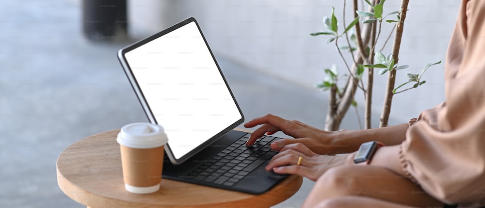 나무 책상에 컴퓨터 태블릿으로 인터넷을 서핑하는 잘린 여자.
