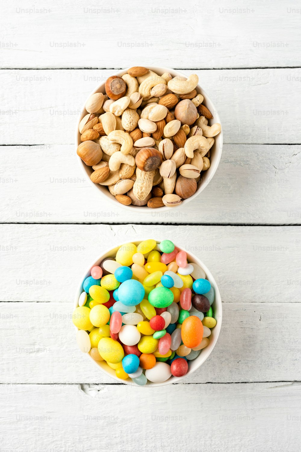 Alimentos saludables vs no saludables. Mezcla de frutos secos y caramelos en cuencos sobre fondo de madera blanca. Vista superior