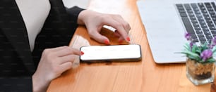 Abgeschnittene Aufnahme einer Frau mit Smartphone auf Holzschreibtisch.