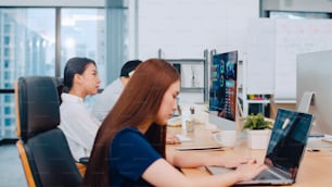 Groupe de processus collaboratif de gens d’affaires multiculturels en tenue décontractée élégante communiquant et utilisant la technologie tout en travaillant ensemble dans un bureau créatif. L’équipe asiatique de jeunes professionnels travaille.