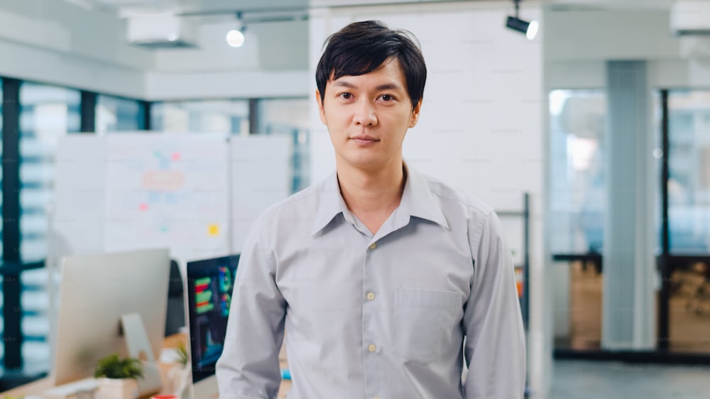Porträt eines erfolgreichen, gutaussehenden Geschäftsmannes Smart Casual Wear, der in die Kamera schaut und lächelt, die Arme am modernen Büroarbeitsplatz verschränkt. Junger Asiate steht im modernen Besprechungsraum.
