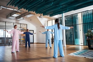 Group of young women standing in a spacious room and putting hands up during their qigong lesson