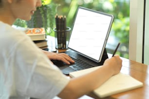 Side view of female teenager doing home work with stationery and digital tablet with mock-up screen