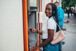 Donna afroamericana allegra che usa la carta di credito e preleva contanti al bancomat