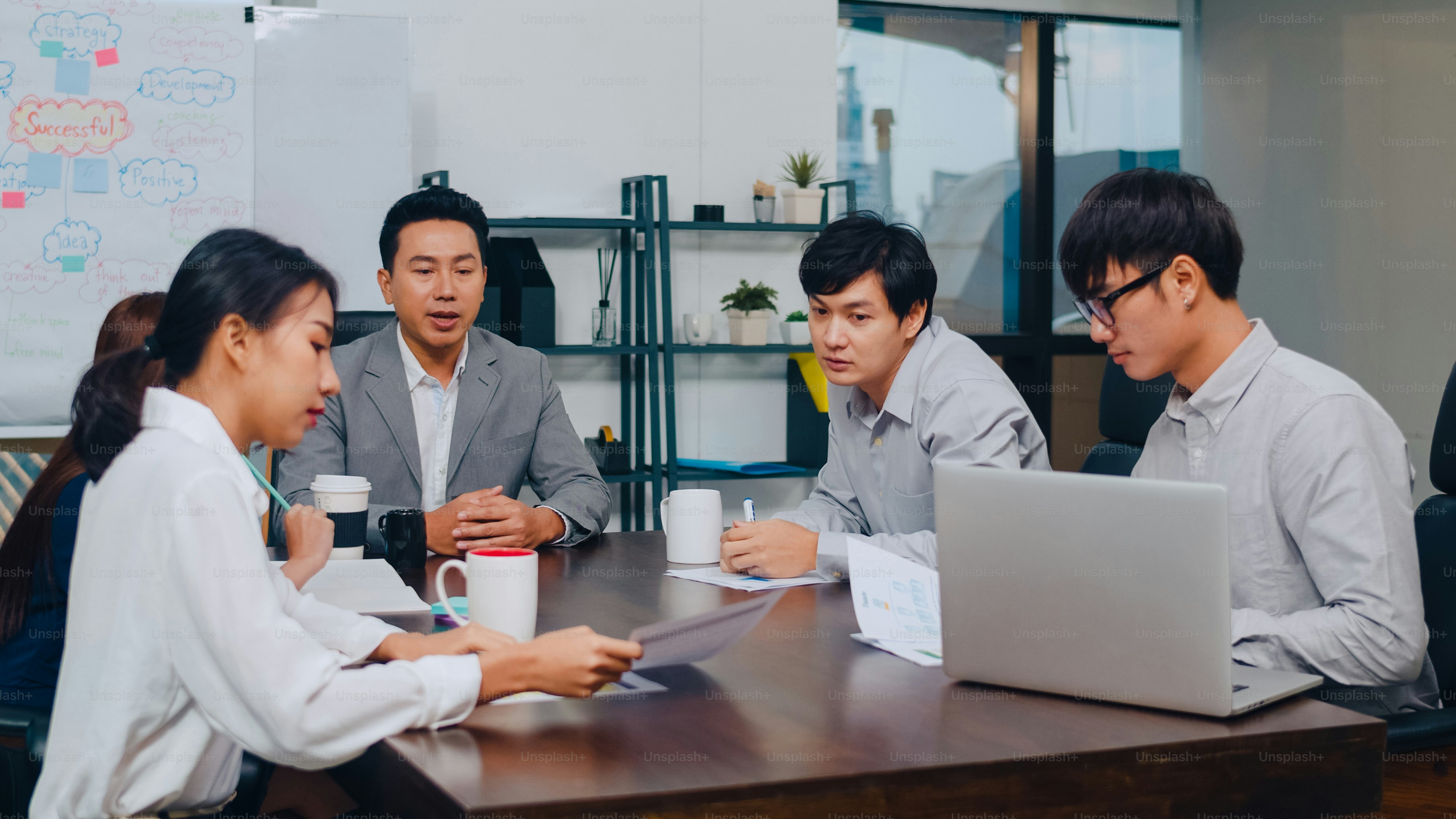 Millennial Asia businessmen and businesswomen meeting brainstorming ideas about new paperwork project colleagues working together planning success strategy enjoy teamwork in small modern night office.