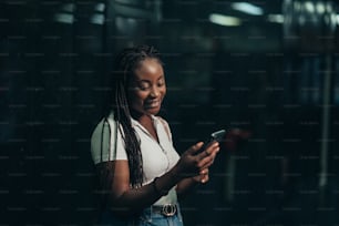 Cheerful african american woman using smartphone while in a subway metro platform at night