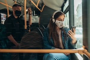 Young woman wearing protective mask and using smartphone while riding a bus during a covid19 pandemic