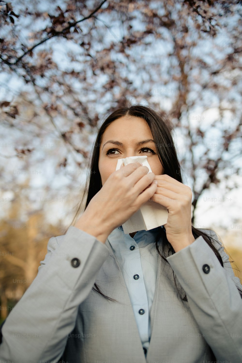 Elegante mujer de negocios que sufre de alergia o gripe estacional de pie en el parque de la ciudad tosiendo y estornudando en el pañuelo facial.
