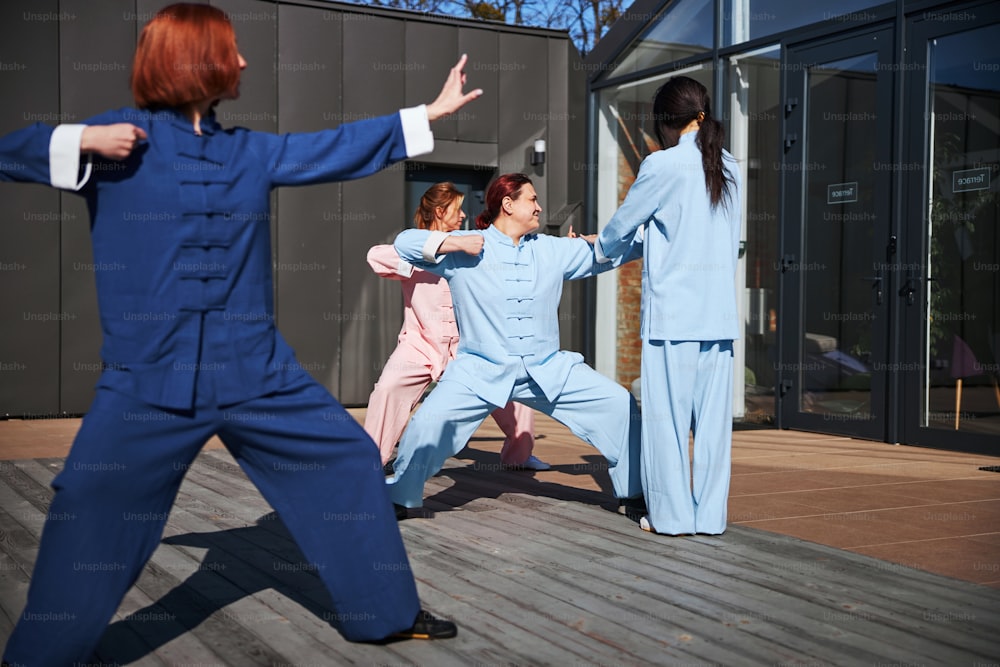 Confident enthusiastic ladies practicing traditional Chinese martial arts outdoors on sunny day