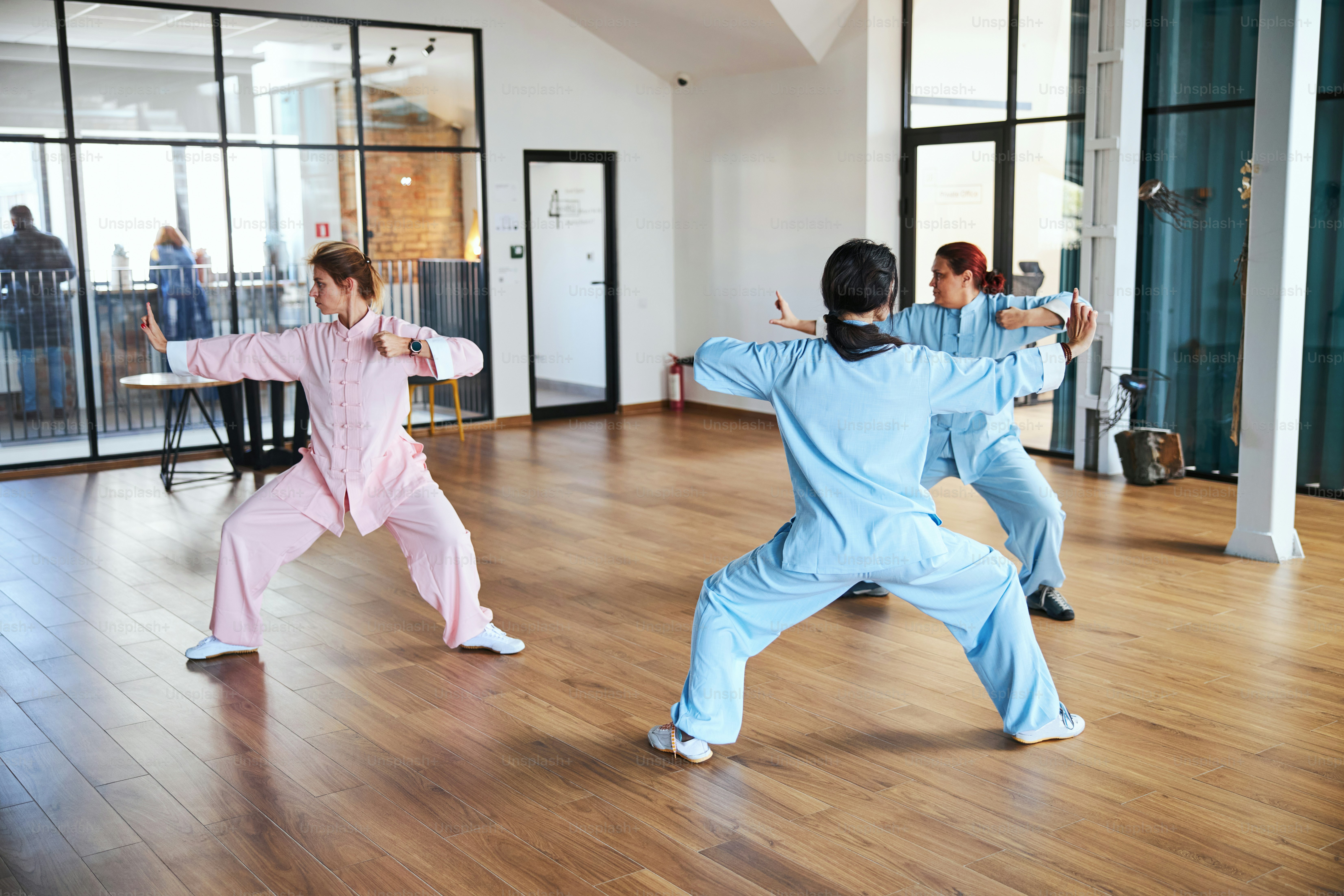Group of women in colorful Chinese suits standing in peculiar postures and practicing tai chi