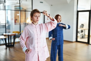 Calm women wearing traditional Chinese clothe standing in specific postures at the qigong class
