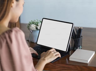 Nahaufnahme einer Frau bei der Arbeit mit digitalem Tablet mit Mock-up-Bildschirm auf Holztisch