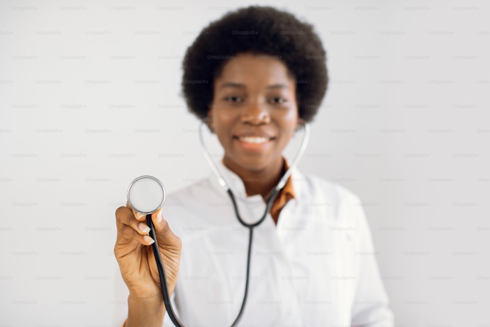 Fokus auf Stethoskop. Unscharfe Nahaufnahme Porträt eines glücklichen afroamerikanischen Arztes, der im Krankenhaus arbeitet und mit Stethoskop posiert. Mensch, Beruf, Gesundheits- und Medizinkonzept