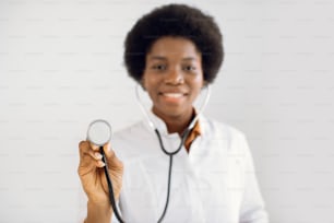 Focus on stethoscope. Blurred close up portrait of happy African American doctor working in hospital, posing with stethoscope. People, occupation, healthcare and medical concept