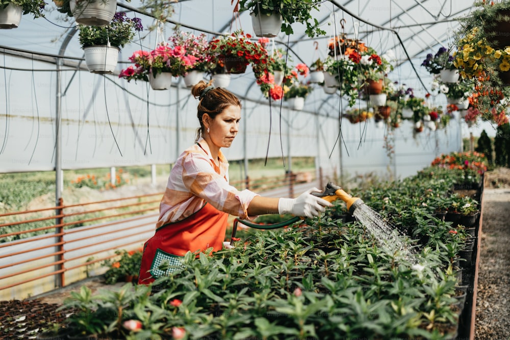 Happy and positive young adult woman working in greenhouse and enjoying in beautiful flowers.
