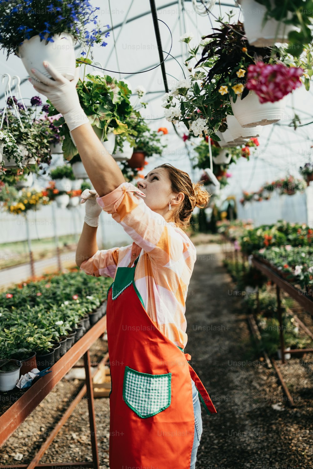 Happy and positive young adult woman working in greenhouse and enjoying in beautiful flowers.