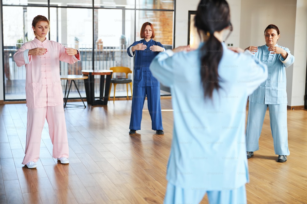 Three calm ladies standing in front of their qigong master and putting hands forward when doing breathing exercises