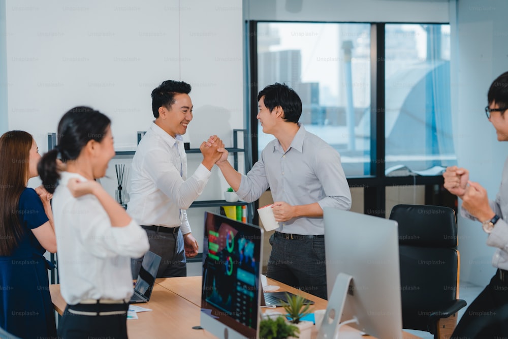 Millennial group of young businesspeople Asia businessman and businesswoman celebrate giving five after dealing feeling happy and signing contract or agreement at meeting room in small modern office.