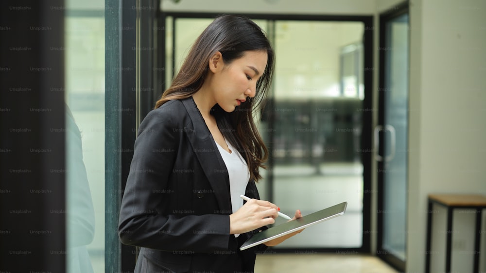 Retrato de vista lateral de una mujer de negocios que usa una tableta digital mientras se relaja en un edificio de oficinas