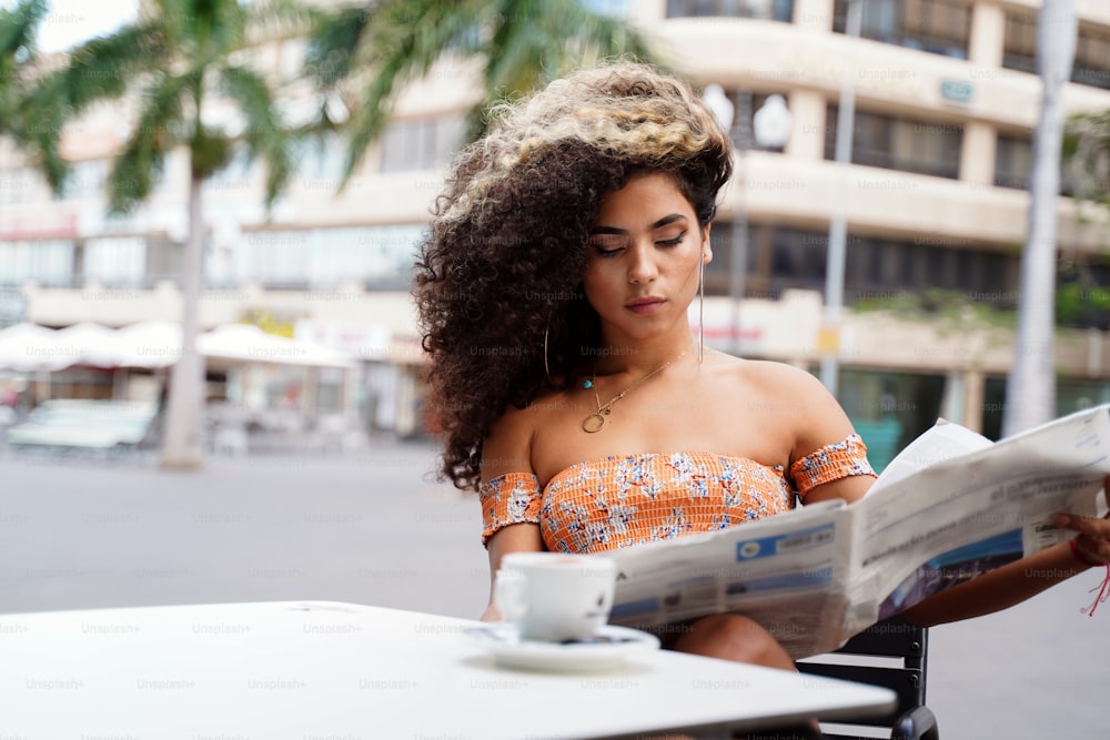 Beautiful afro woman reading magazine and drinking coffee , relax time at cafe. Sunny day.