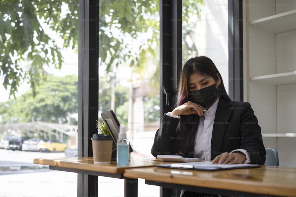 Mujer de negocios segura de sí misma con máscara protectora analizando datos financieros en la oficina.