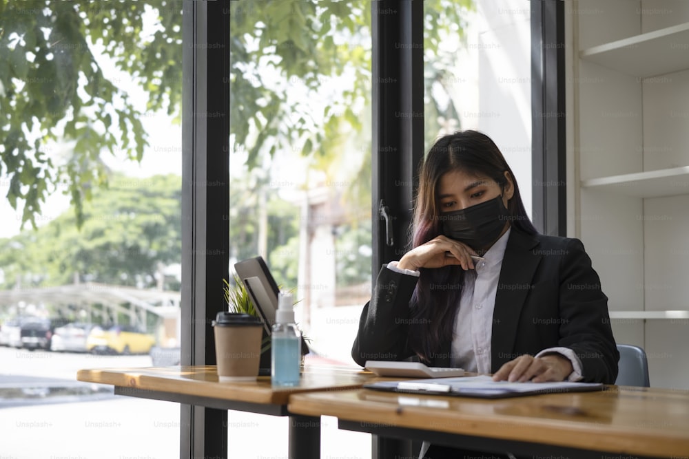 Donna d'affari fiduciosa in maschera protettiva che analizza i dati finanziari in ufficio.