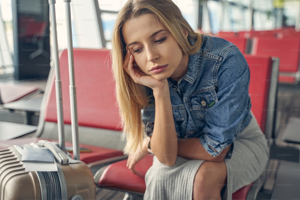 Young female person sitting in lounge zone of the airport and leaning elbow on knee
