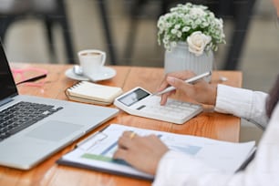 Foto recortada de una mujer de negocios usando una calculadora y analizando un documento financiero en un escritorio de madera.