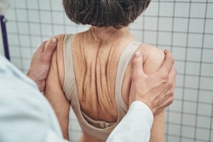 Cropped photo of a male physical therapist squeezing the patient shoulders during a postural assessment