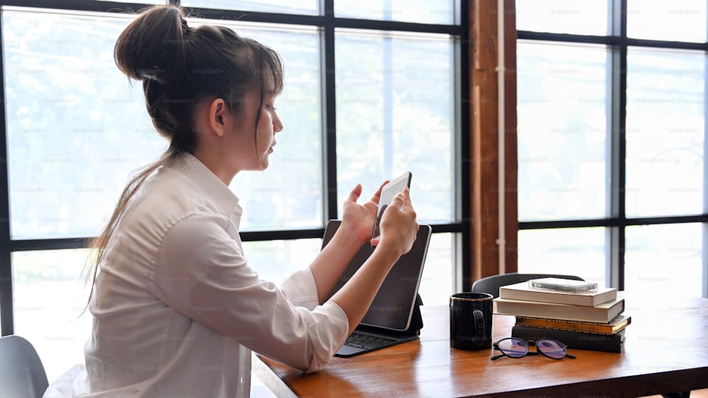 Vista lateral de una mujer joven sentada en una cafetería y jugando juegos en línea en un teléfono inteligente.