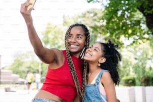 Mãe e filha afro-americanas desfrutando de um dia ao ar livre enquanto tiram uma selfie com um telefone celular na rua.