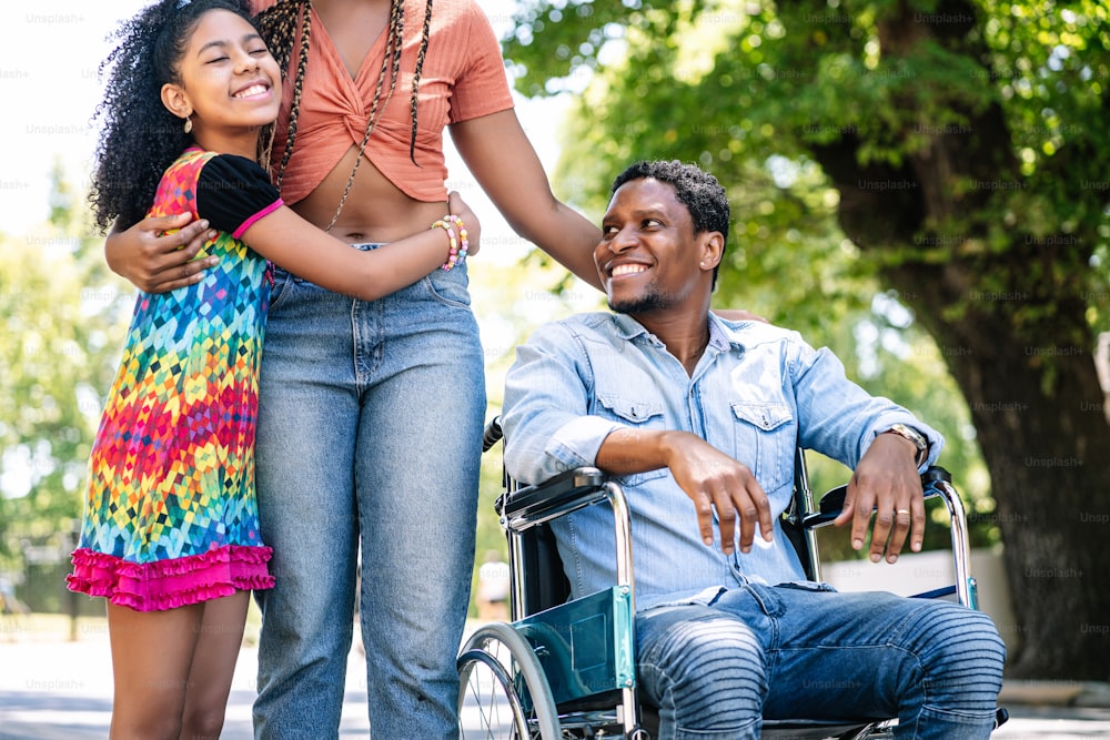 An african american man in a wheelchair enjoying a walk outdoors on the street with his family.