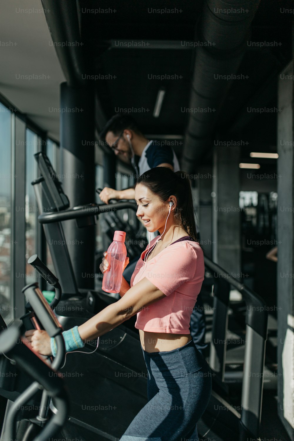 Homem e mulher jovens em forma correndo na esteira no ginásio de fitness moderno.