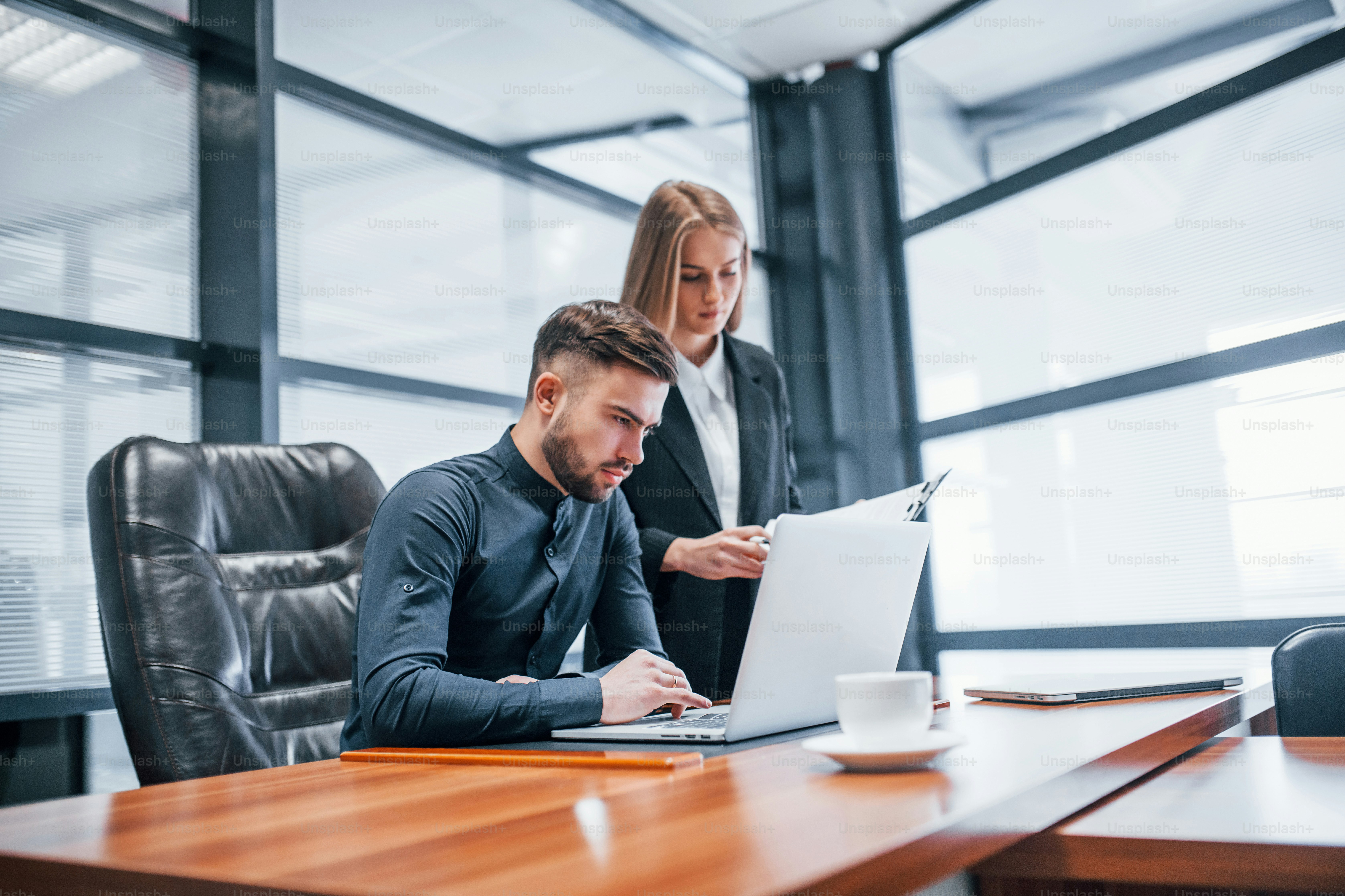 Woman and man in formal clothes working together indoors in the office by table.