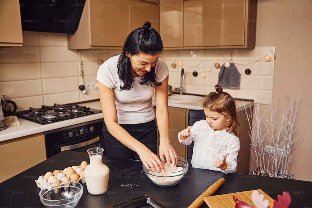 Mamma con la sua piccola figlia che prepara il cibo in cucina e si diverte.